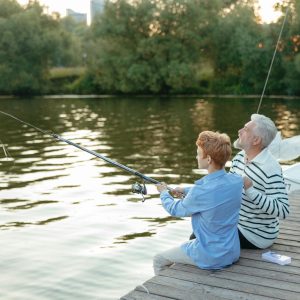 An elderly man and young man enjoy a serene fishing experience on a lakeside dock.