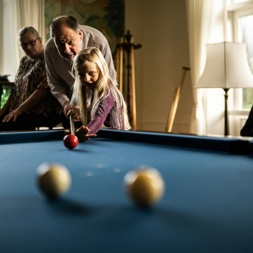 A young girl playing billiards with her supportive grandparents indoors.
