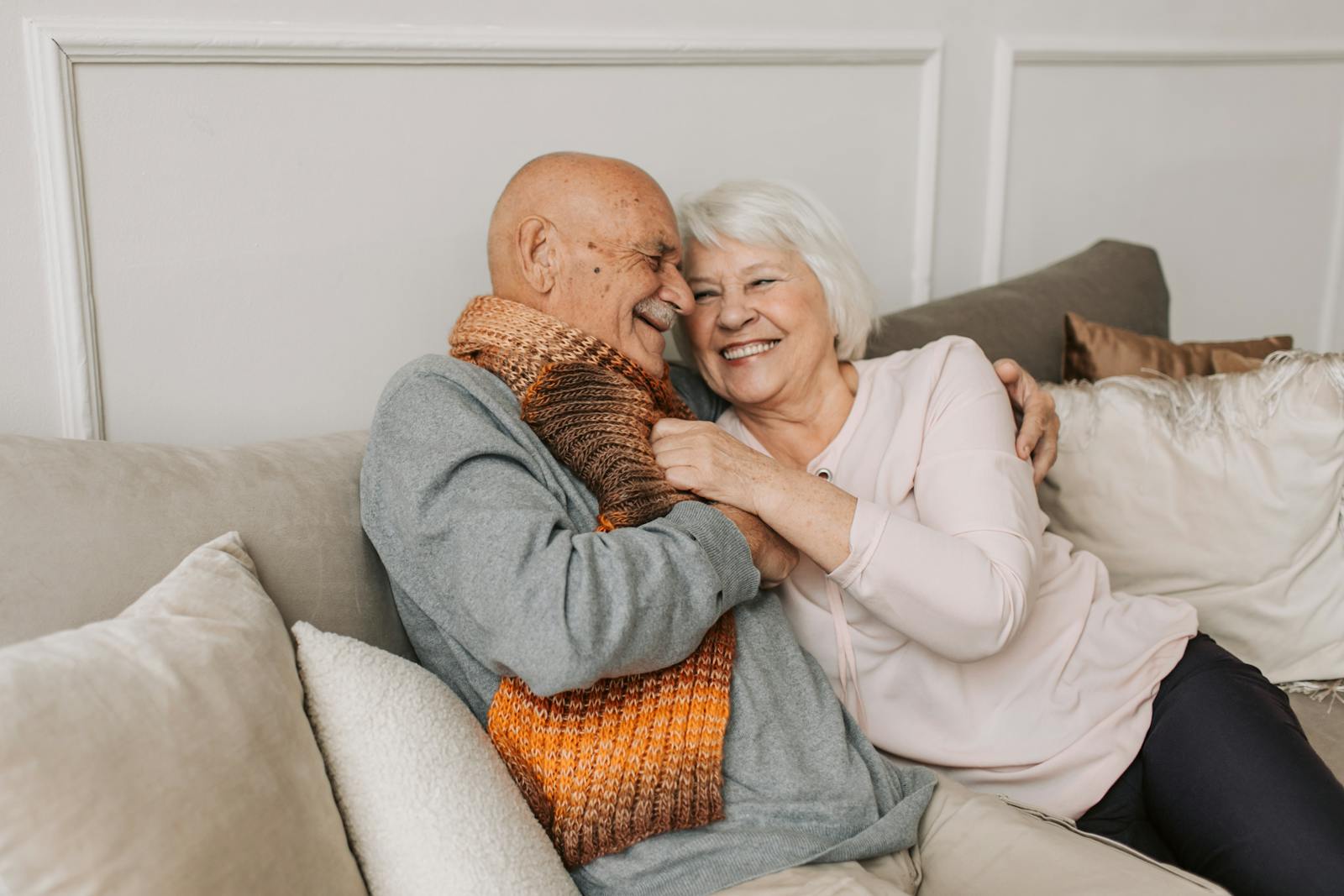 Happy elderly couple embraced in a cozy home setting, sharing joyful smiles.